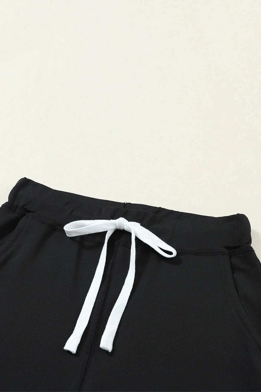 Black jogger pants with white drawstring and elastic waistband on neutral background