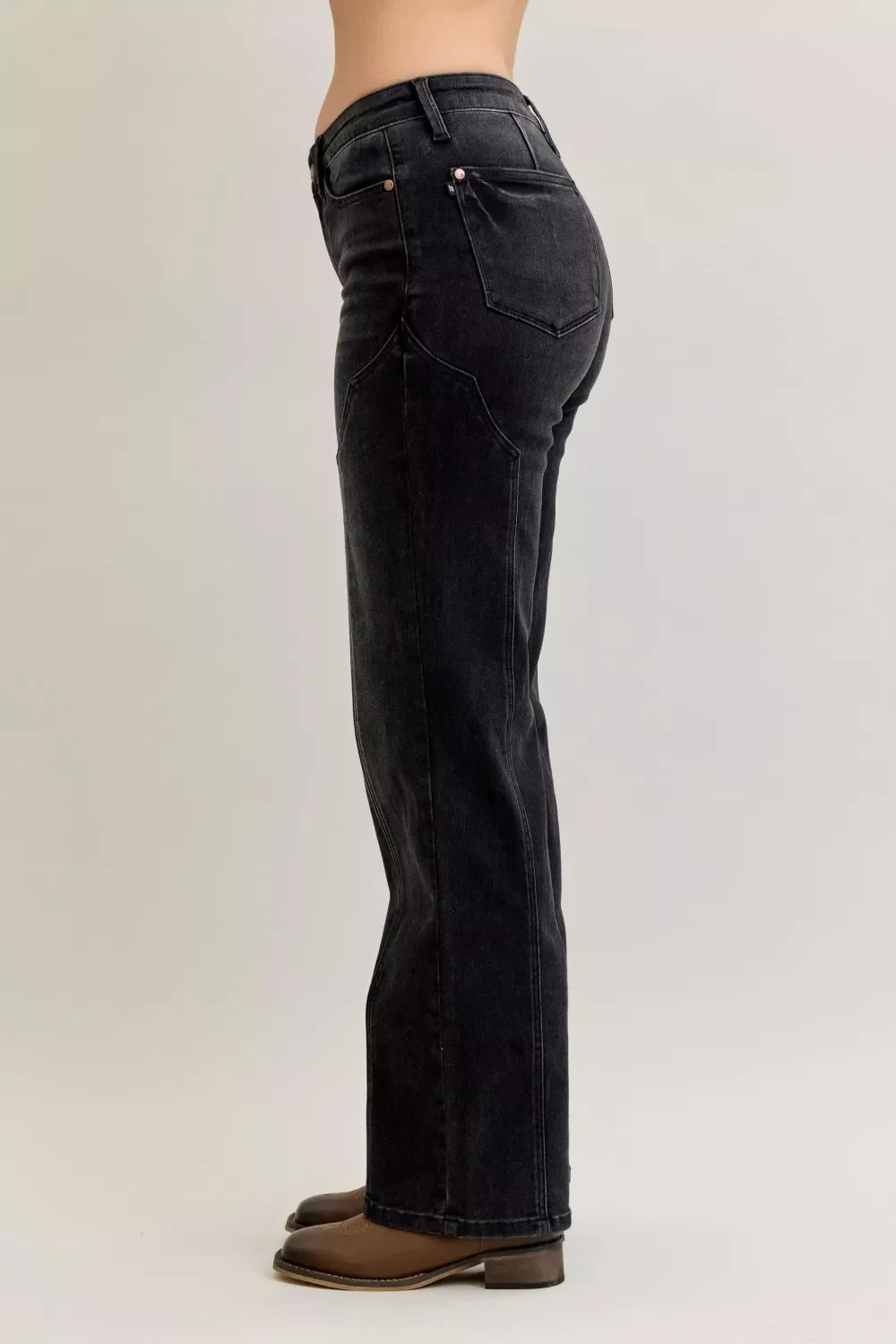 Side view of black high-waisted straight leg jeans with brown boots on a model
