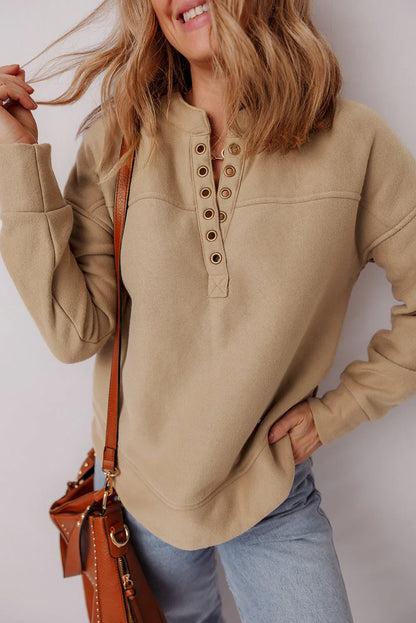 Woman in a beige henley pullover, light wash jeans, and brown shoulder bag