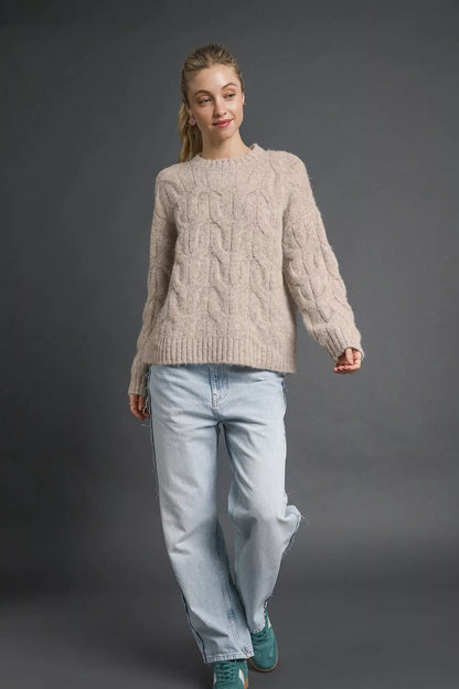 Woman in a chunky cable knit sweater, light wash jeans, and teal sneakers, studio background