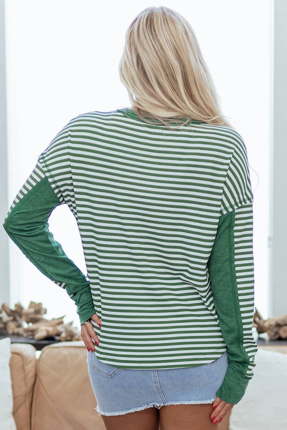 Woman wearing green and white striped long sleeve top with denim shorts, back view.