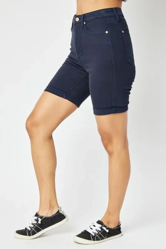 Woman wearing high-waisted navy denim Bermuda shorts and black casual sneakers