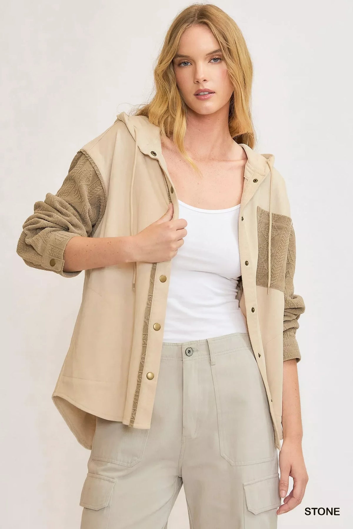 Woman wearing a beige hooded jacket with textured sleeves and front pocket, paired with cargo pants.