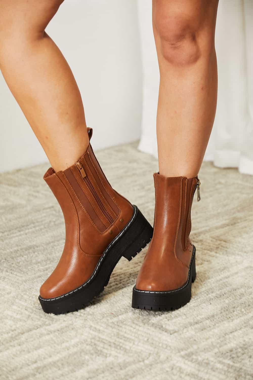 Woman wearing brown leather ankle boots with chunky black soles on a neutral carpet