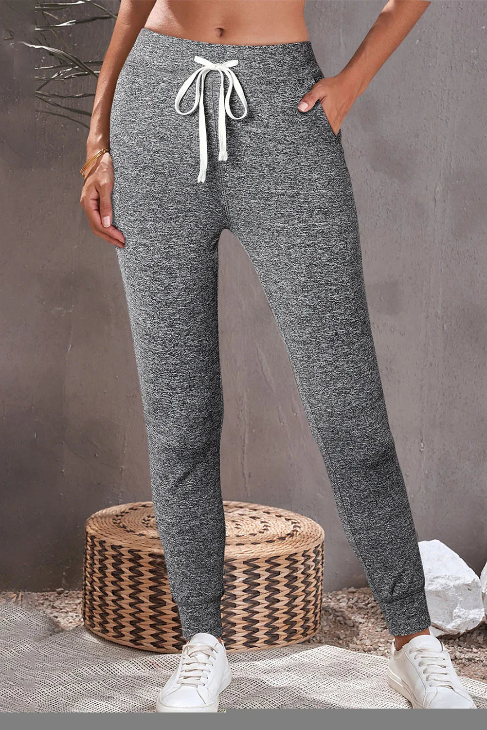 Woman wearing grey jogger sweatpants with drawstring and pockets, styled with white sneakers.