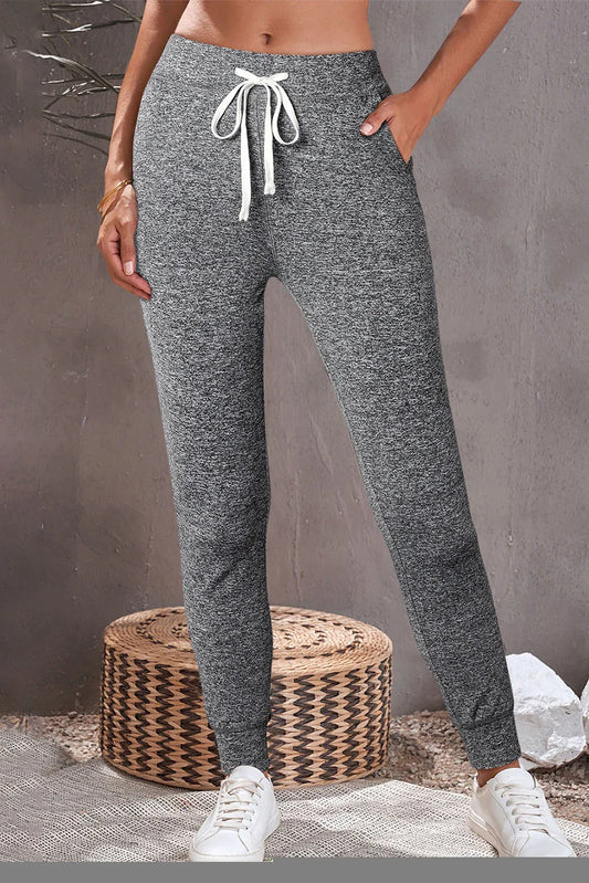 Woman wearing grey jogger sweatpants with drawstring and pockets, styled with white sneakers.