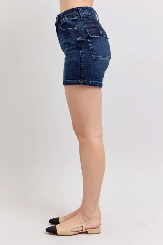 Woman wearing high-waisted dark denim shorts with side pocket, shown in side profile.