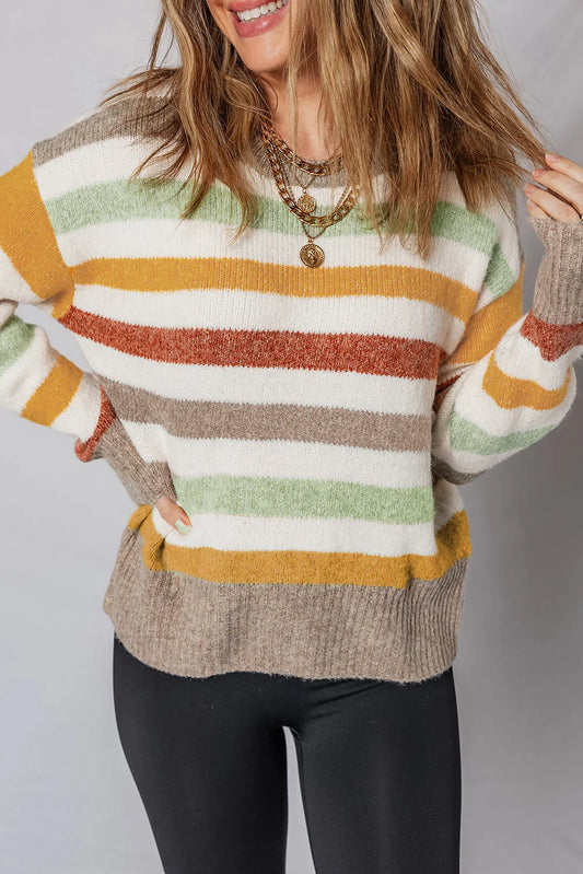 Woman wearing a cozy striped sweater in green, mustard, rust, and beige with black leggings