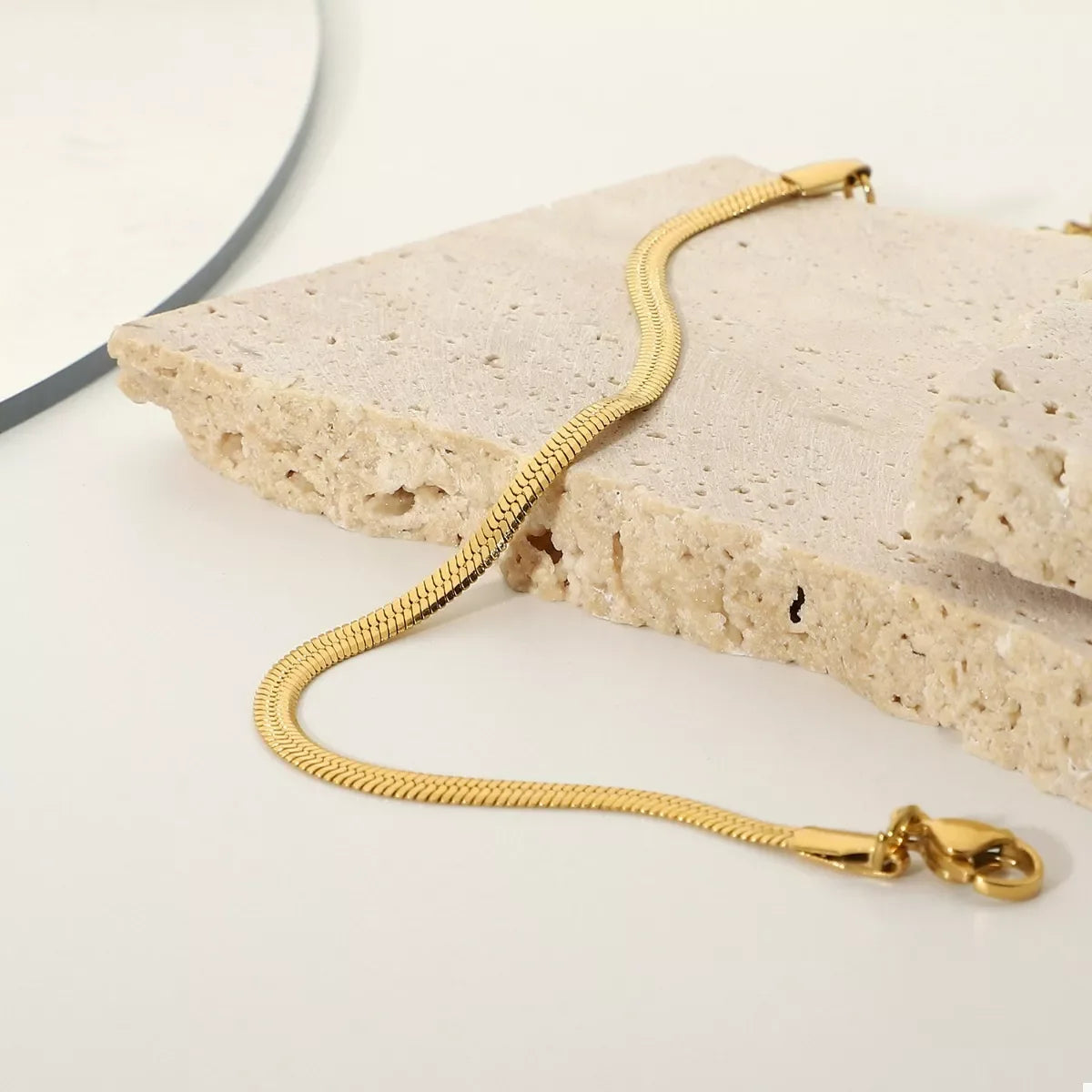 Gold snake chain bracelet displayed on textured stone for modern jewelry styling