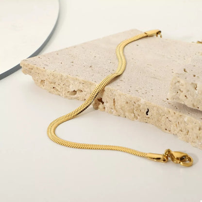 Gold snake chain bracelet displayed on textured stone for modern jewelry styling