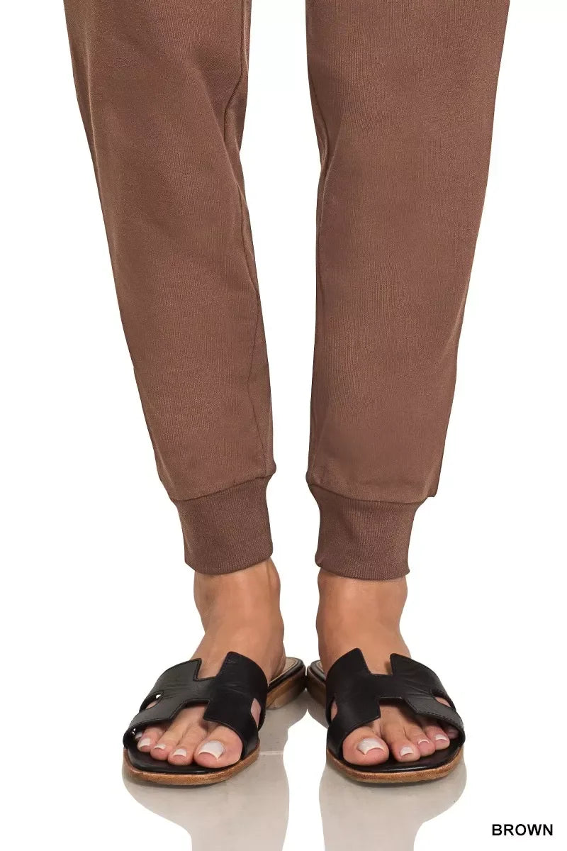 Brown jogger pants paired with black slide sandals on a white background