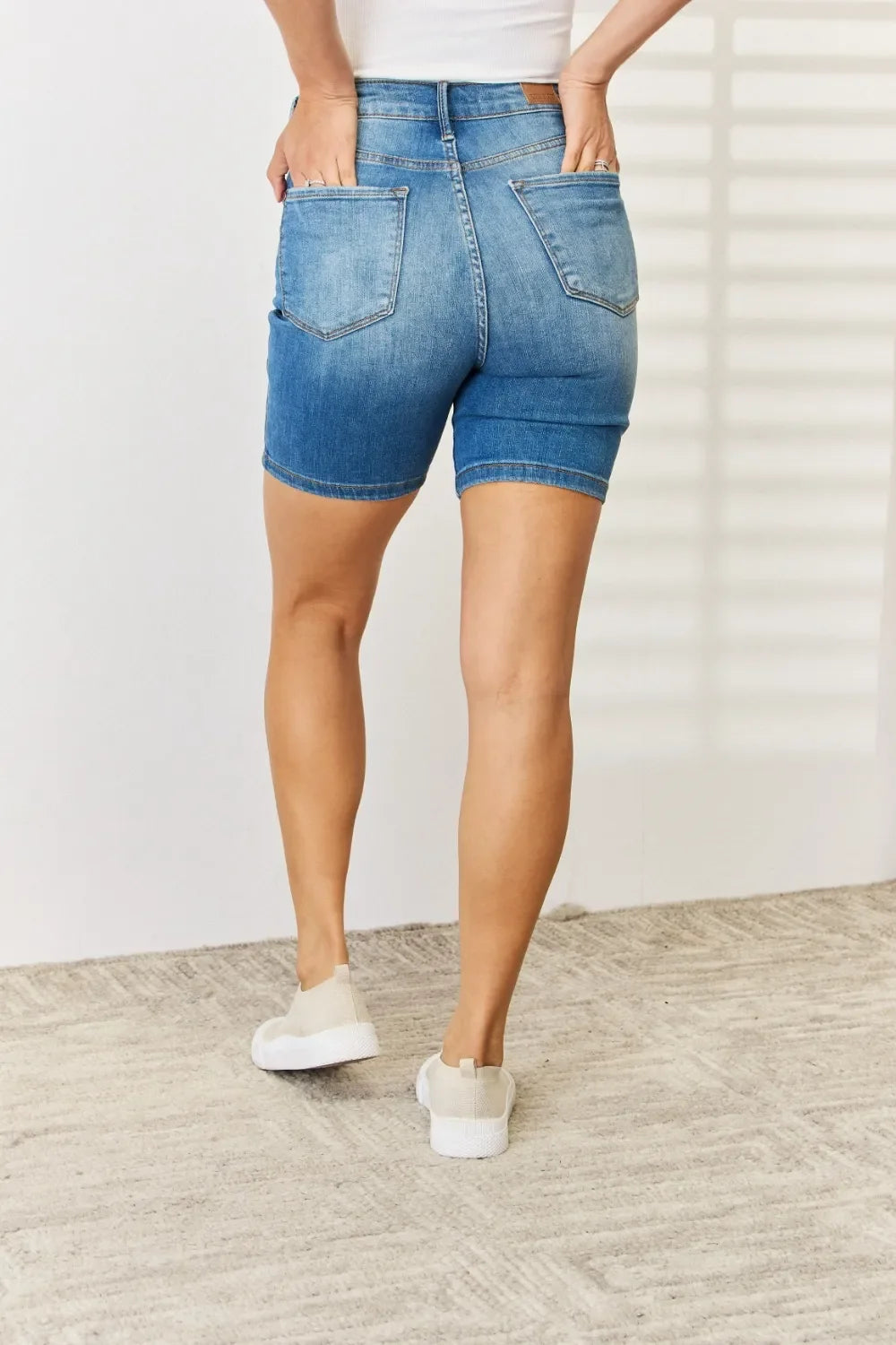 Back view of woman wearing high-waisted denim shorts and casual white sneakers indoors