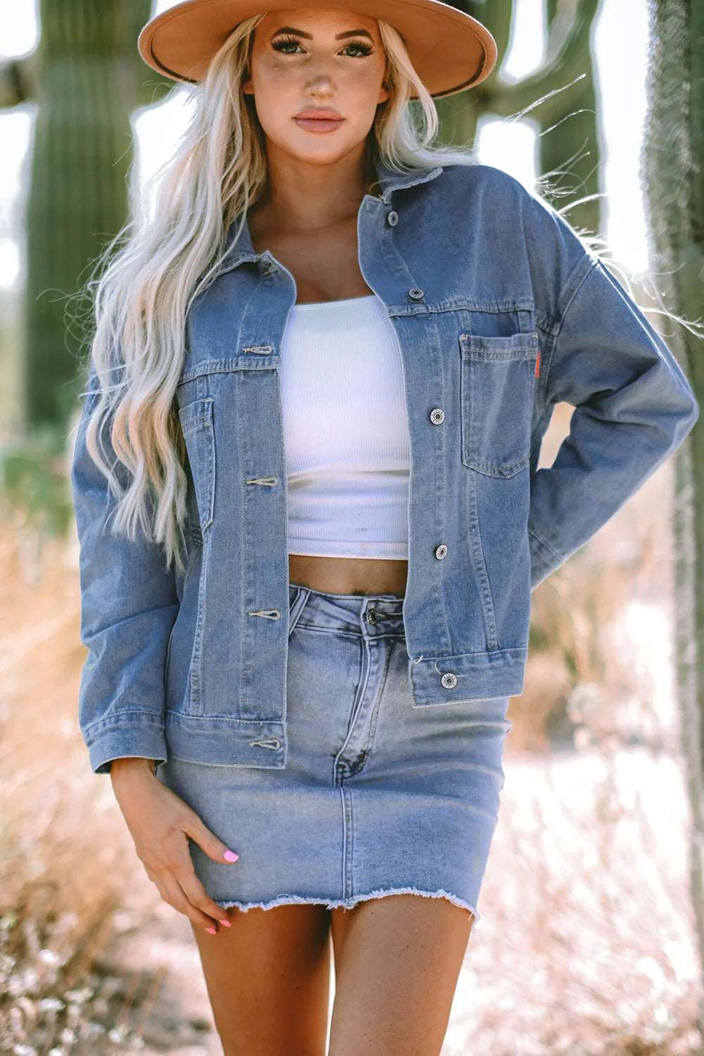 Woman outdoors in a denim jacket and denim mini skirt with a white crop top and wide-brim hat