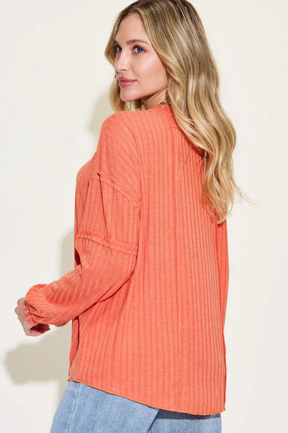 Woman wearing a relaxed-fit, long sleeve orange ribbed top with light wash jeans.