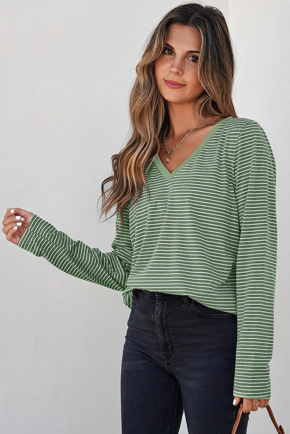 Woman wearing a green striped V-neck long sleeve top with black high-waisted jeans