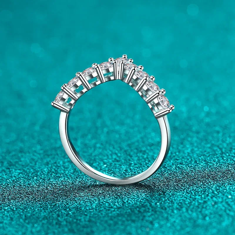 Silver band ring with row of round clear gemstones on a teal textured background.