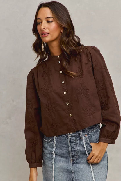 Woman wearing a brown embroidered button-up blouse with long sleeves and a high collar, paired with a denim skirt.