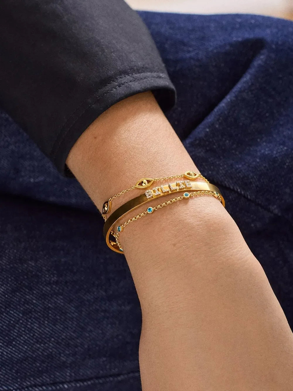 Gold bracelets with turquoise accents on wrist, paired with casual dark clothing