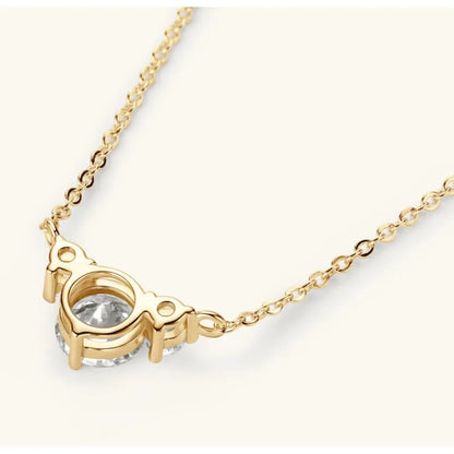 Gold chain necklace with a round clear gemstone center pendant on a cream background