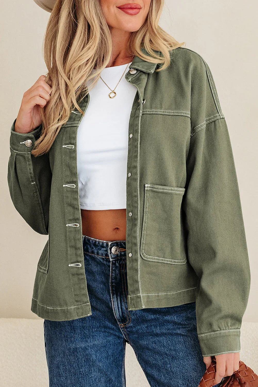 Woman wearing olive green overshirt, white crop top, blue jeans, and gold necklace