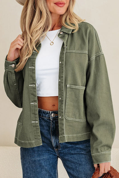 Woman wearing olive green overshirt, white crop top, blue jeans, and gold necklace