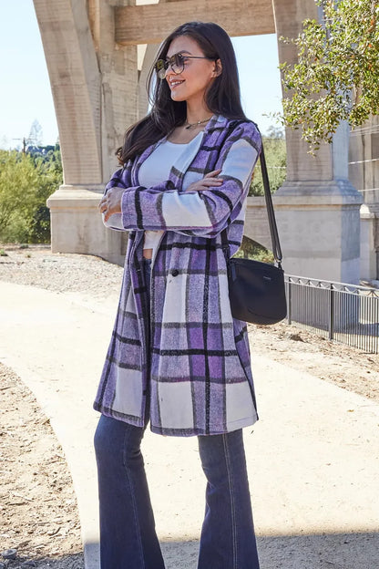 Woman in purple plaid coat, white top, and flared jeans standing outdoors in sunlight.
