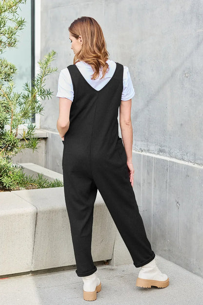 Woman wearing a black sleeveless jumpsuit over a white tee with chunky boots outside