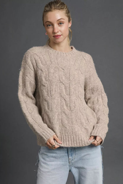Woman wearing a relaxed fit cable knit stone sweater with light wash jeans