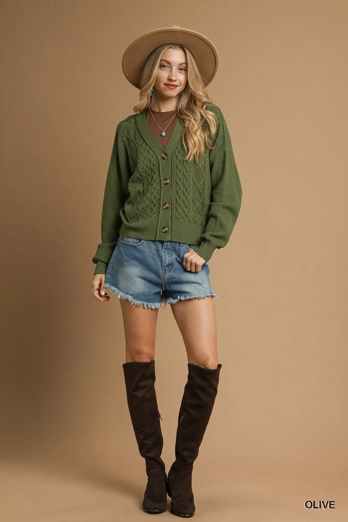Woman wearing a green cardigan, denim shorts, and brown knee-high boots on a beige background