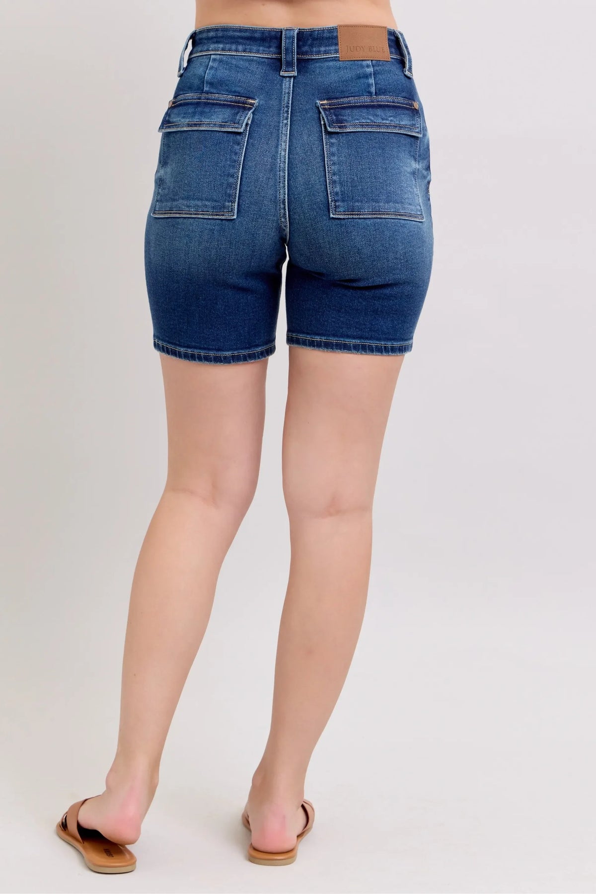 Back view of high-waisted denim shorts with large patch pockets, worn by a woman in sandals.