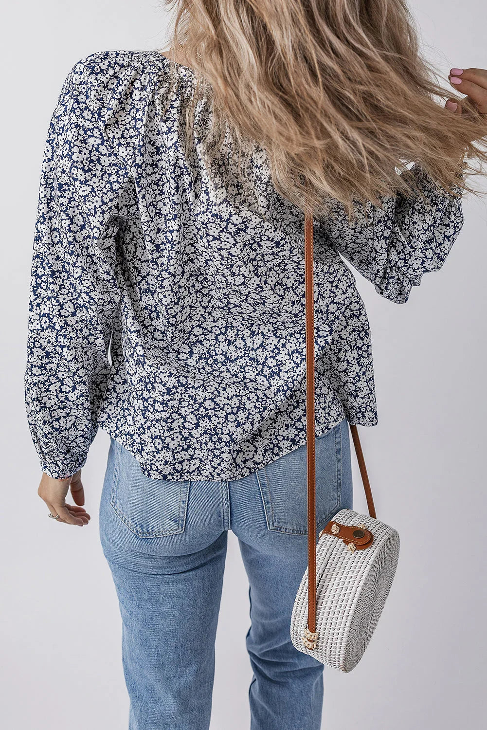 Woman in blue floral blouse and light wash jeans carrying white round woven crossbody bag