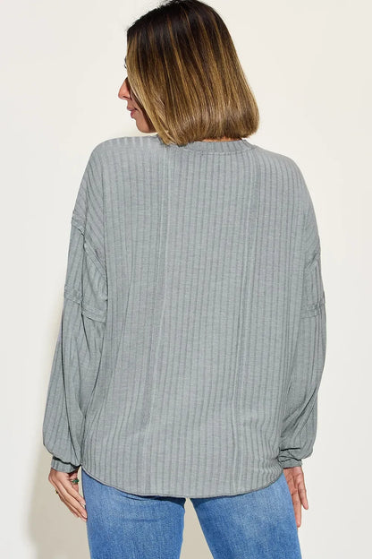 Back view of woman wearing a grey ribbed long sleeve blouse and blue jeans.