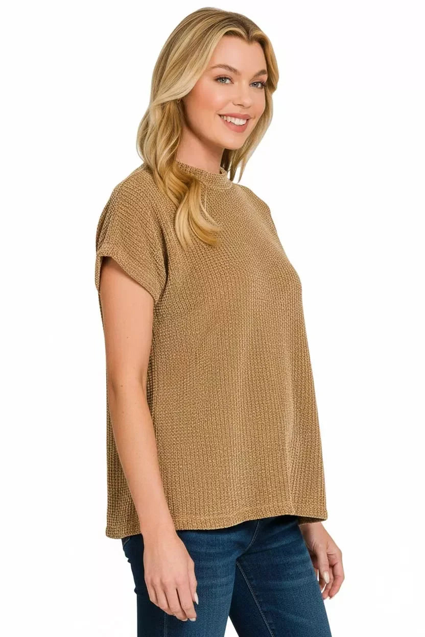 Woman wearing a loose-fit, tan textured knit top with short sleeves and blue jeans.