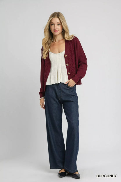 Woman wearing burgundy knit cardigan, white textured top, and wide-leg dark jeans.