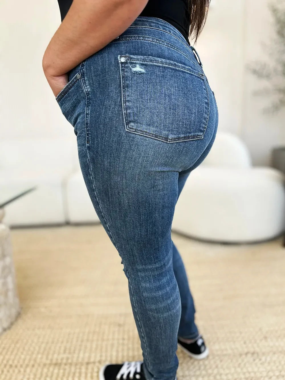 Woman wearing mid-rise blue skinny jeans with back pocket detail, hands in pockets