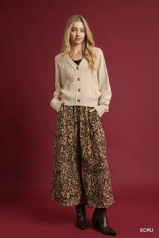 Woman wearing a beige cable knit cardigan and wide-leg leopard print pants with boots