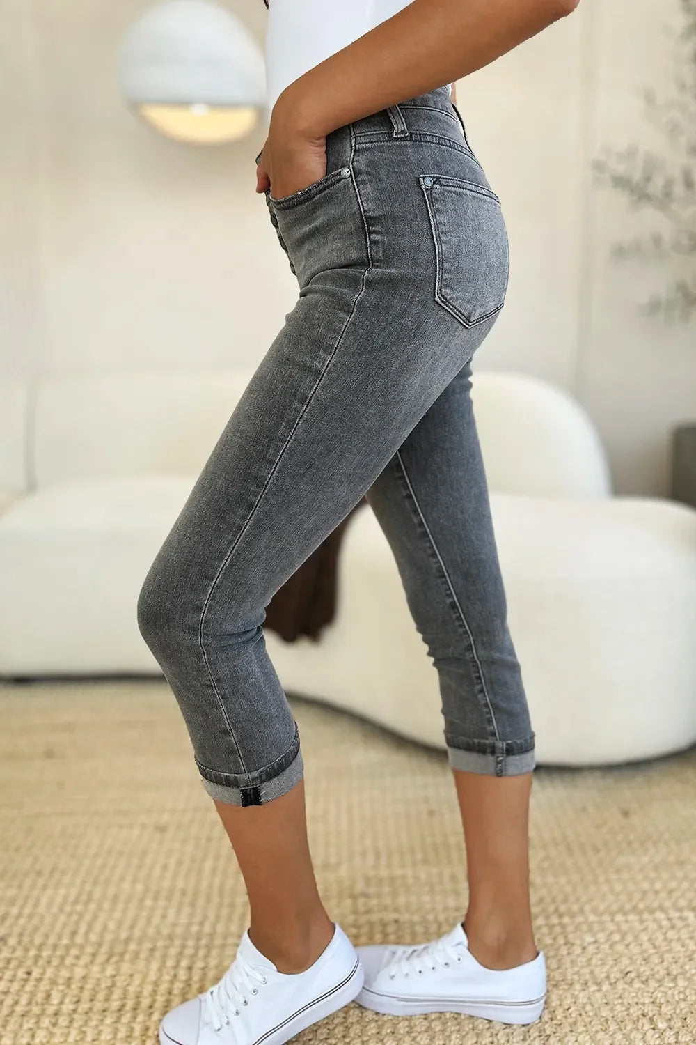 Woman wearing grey cropped skinny jeans and white sneakers in a modern living room