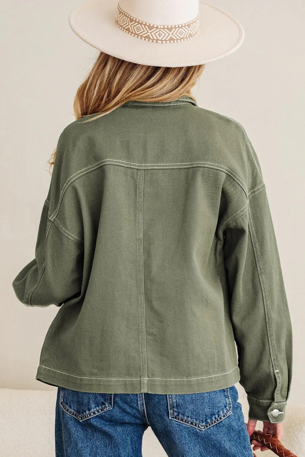 Woman in an olive green relaxed jacket, blue jeans, and cream wide-brim hat, back view