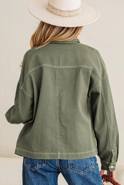 Woman in an olive green relaxed jacket, blue jeans, and cream wide-brim hat, back view