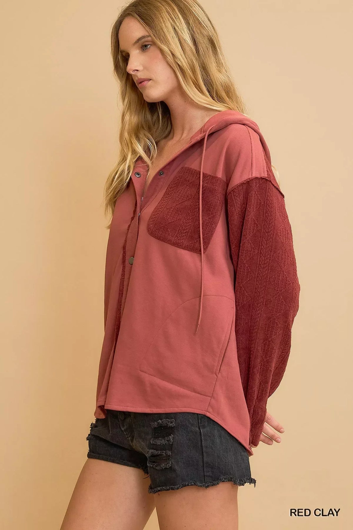 Woman wearing a relaxed red clay hooded button-up shirt with textured sleeves and black denim shorts