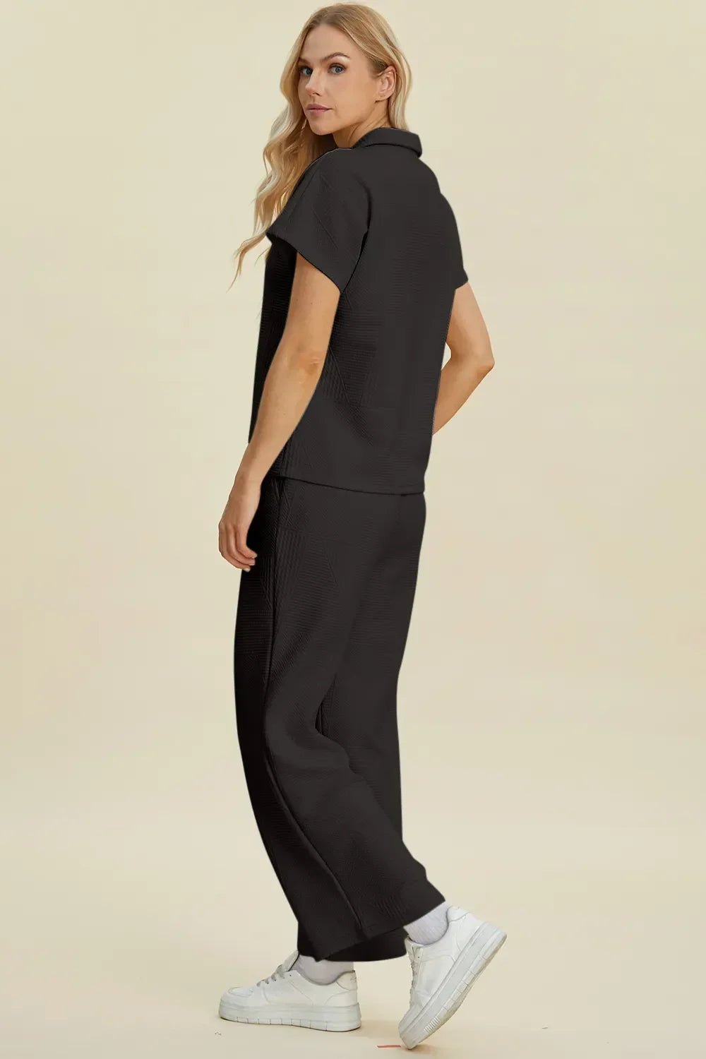 Woman modeling relaxed black short sleeve top and wide leg pants set with white sneakers