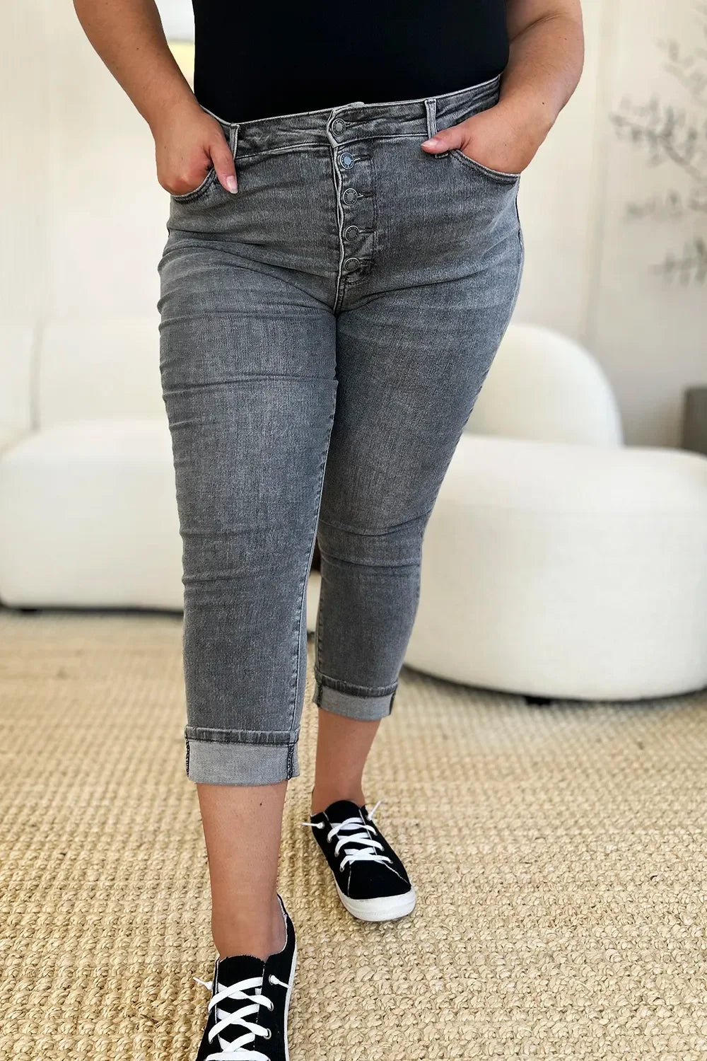 Woman wearing grey high-waisted cropped jeans with button fly and black sneakers