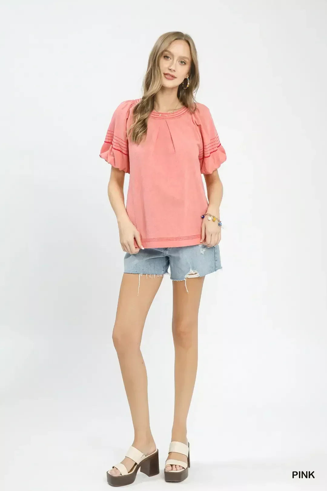 Woman wearing a pink short-sleeve blouse with ruffled sleeves and denim frayed shorts