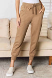 Woman wearing tan jogger pants with drawstring waist, front pockets, and slip-on shoes indoors