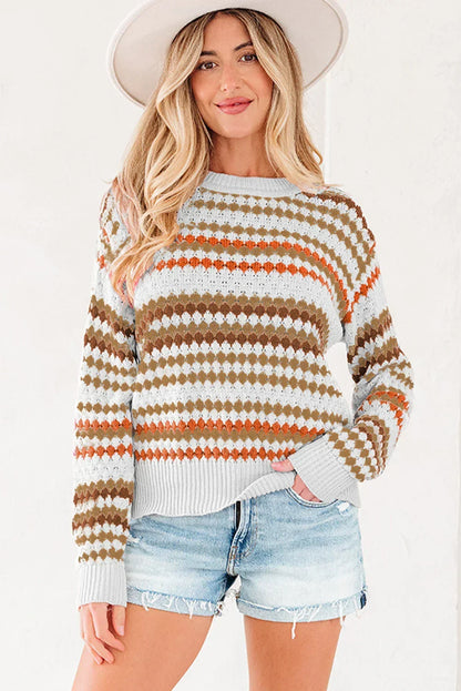 Woman wearing a patterned knit sweater with orange and brown stripes, denim shorts, and a wide-brim hat.