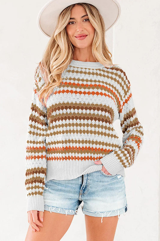 Woman wearing a patterned knit sweater with orange and brown stripes, denim shorts, and a wide-brim hat.