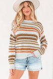 Woman wearing a patterned knit sweater with orange and brown stripes, denim shorts, and a wide-brim hat.