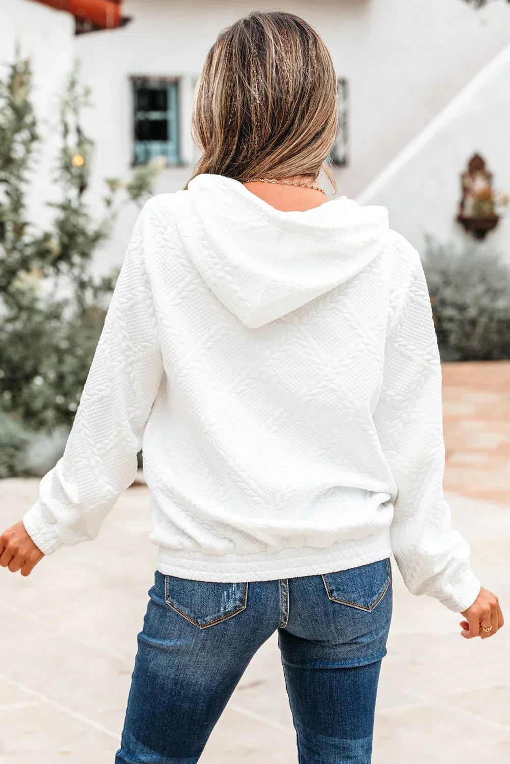 Woman wearing a textured white hooded sweatshirt and blue jeans outdoors