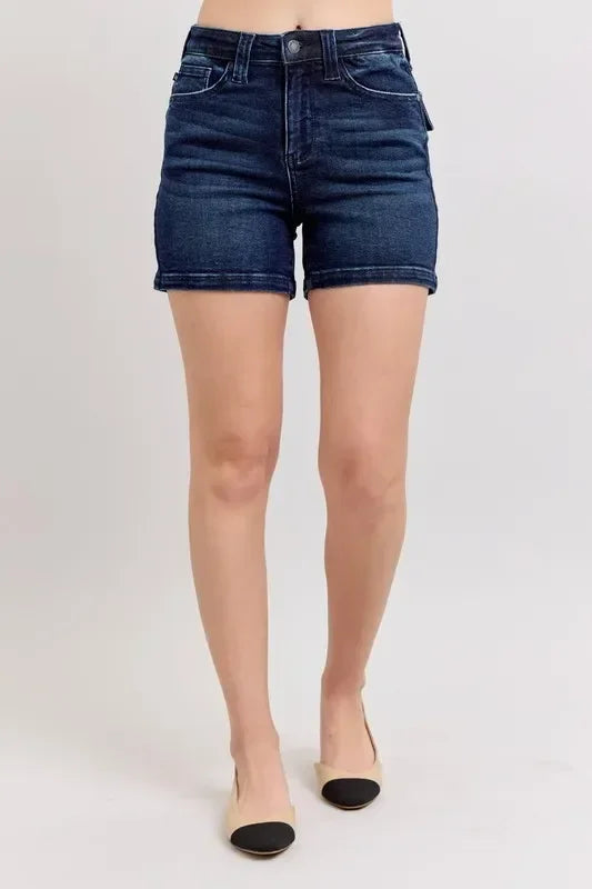 Woman wearing high-waisted dark denim shorts and beige flats on a plain background