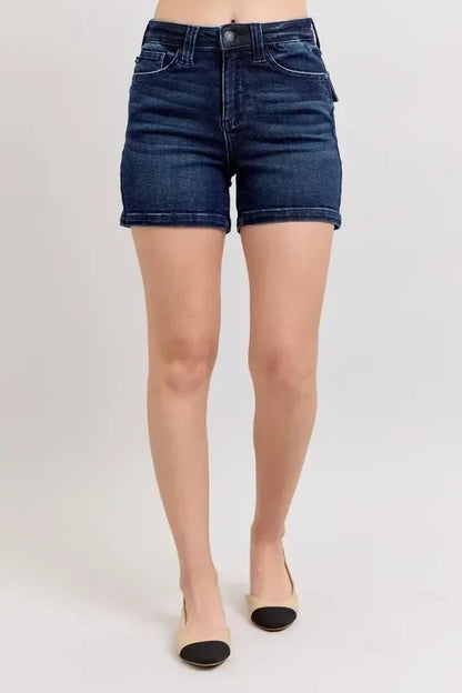 Woman wearing high-waisted dark denim shorts and beige flats on a plain background